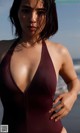 A woman in a maroon swimsuit standing on the beach.