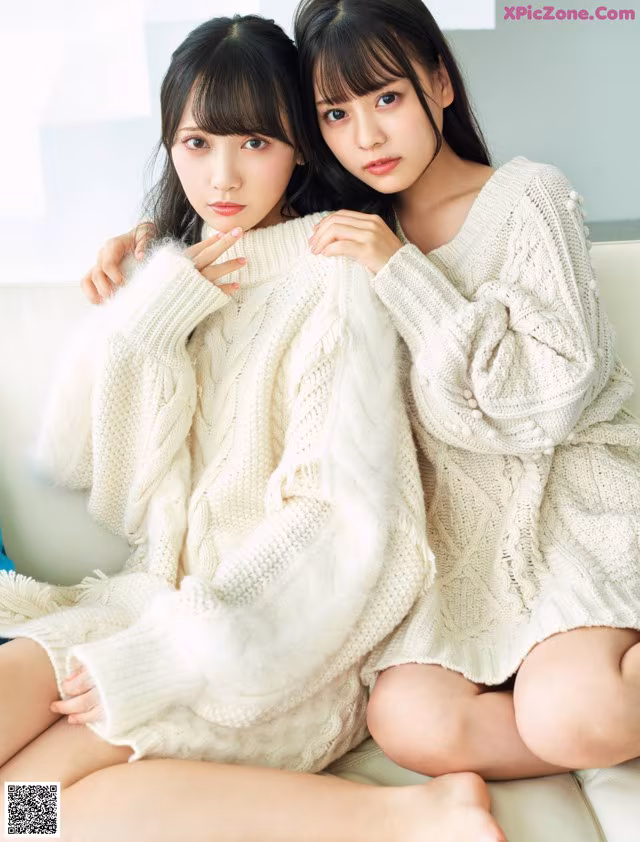 Two young women sitting on a couch wearing white sweaters.