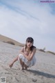 A woman in a white dress sitting on a sandy beach.