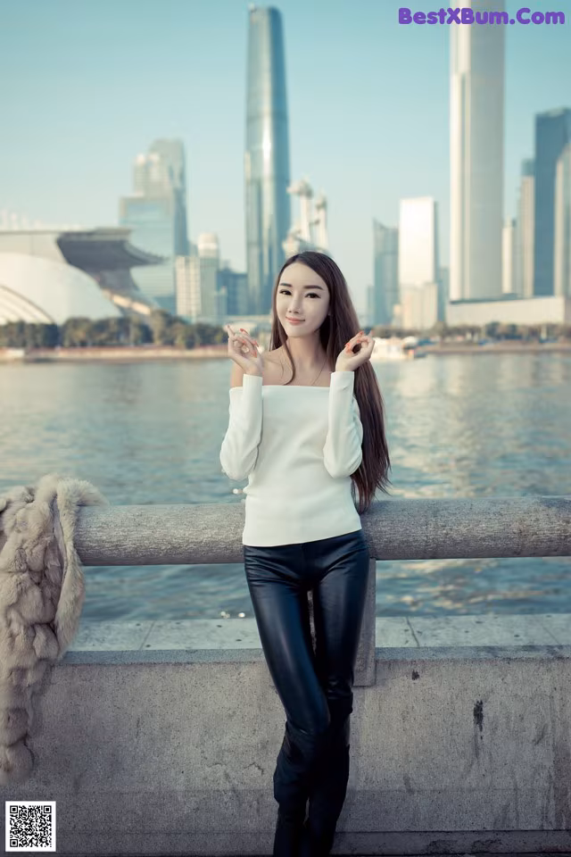 A woman in a white sweater and black pants posing for a picture.