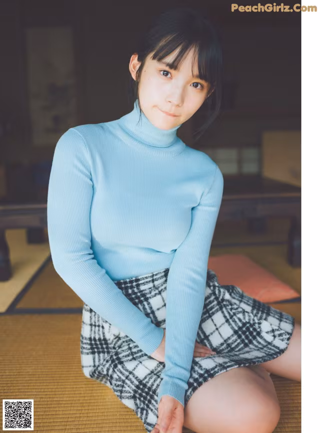 A woman in a blue turtleneck sweater sitting on the floor.