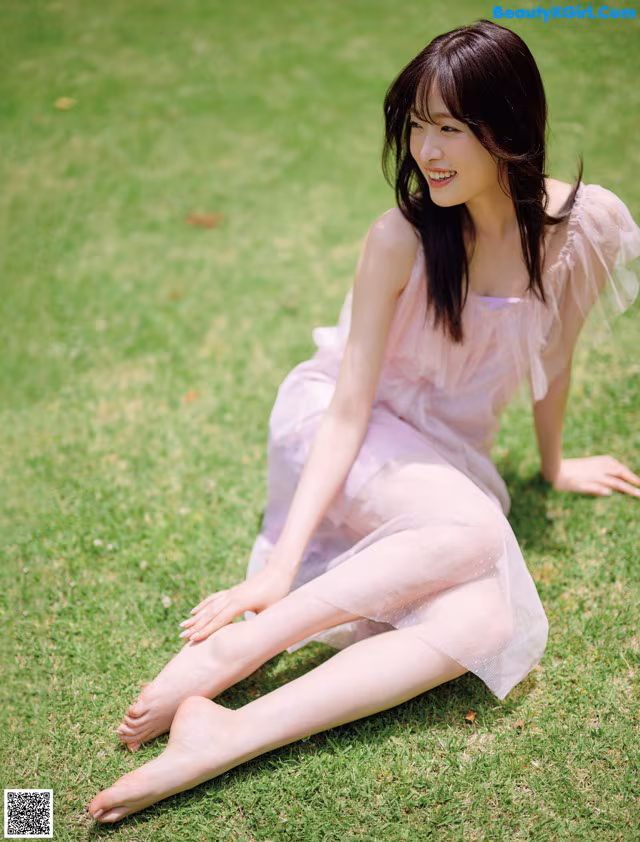 A woman in a pink dress sitting on the grass.
