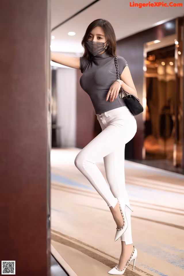 A woman wearing a face mask leaning against a wall.