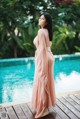 A woman in a pink dress standing by a swimming pool.