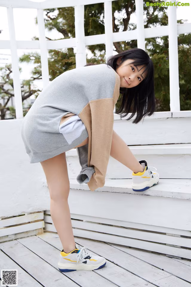 A woman in a gray sweater and white shorts posing on a wooden deck.