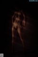 A nude woman standing in a dark room.