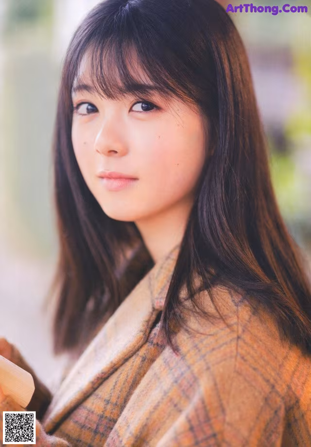 A woman with long brown hair wearing a plaid jacket.