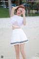 A woman in a white top and skirt standing on a beach.