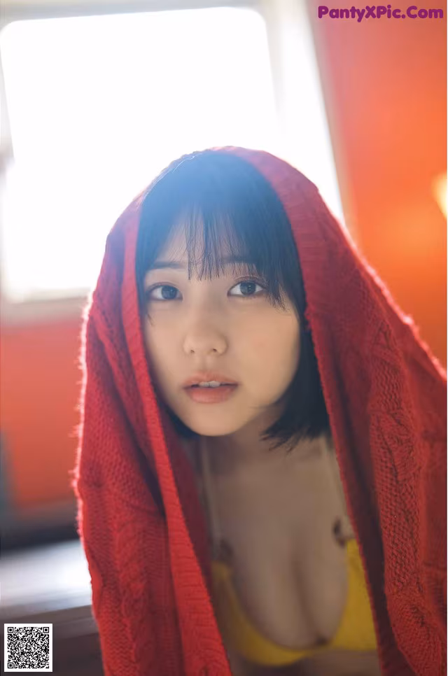 A woman in a yellow bikini under a red blanket.