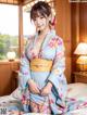 A woman in a blue kimono sitting on a bed.