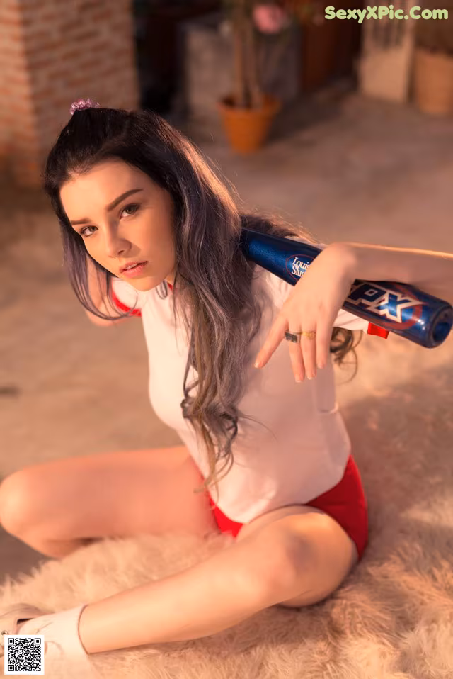 A woman in a white shirt and red shorts holding a baseball bat.