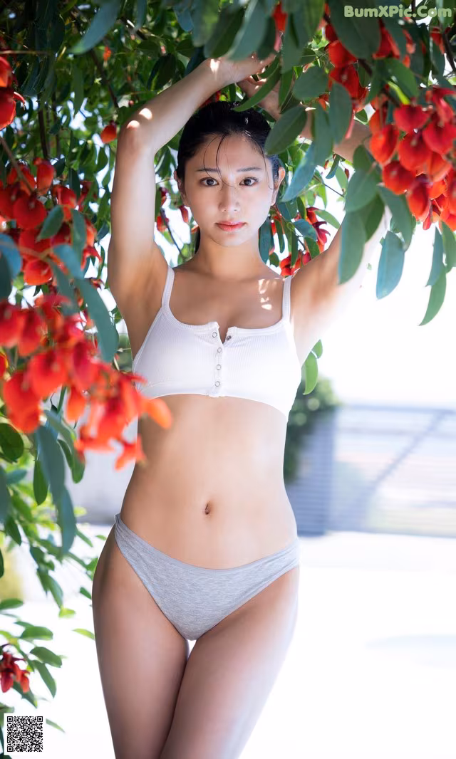 A woman in a white bikini standing under a tree.