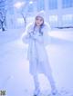 A woman in a white coat and hat standing in the snow.