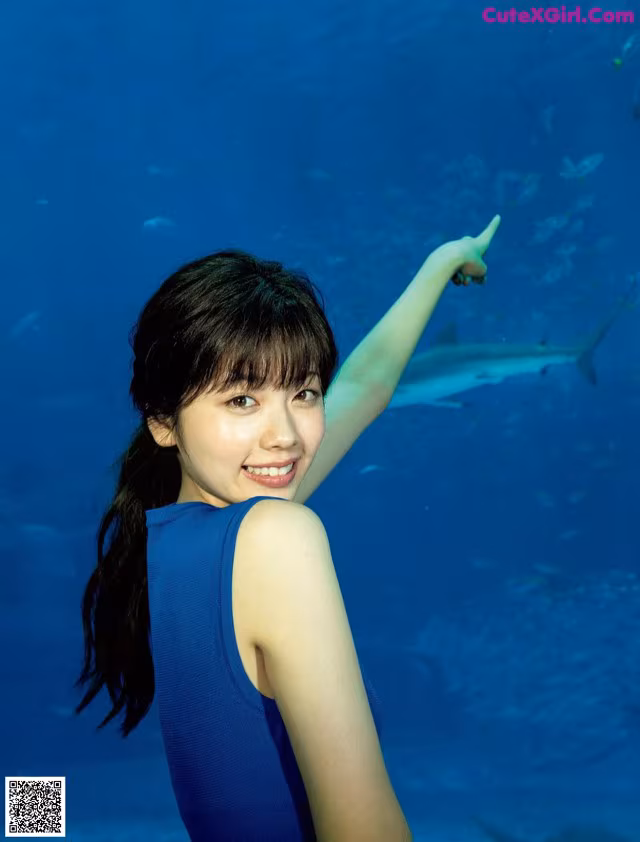 A woman in a blue dress pointing at a shark.
