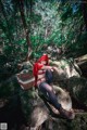 A woman in a red hoodie sitting on a rock in the woods.