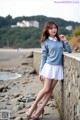 A woman leaning against a stone wall on the beach.