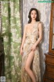 A woman in a gold dress posing in front of a dresser.